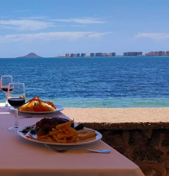 Mesa de restaurante frente al mar con el skyline de La Manga del Mar Menor al fondo