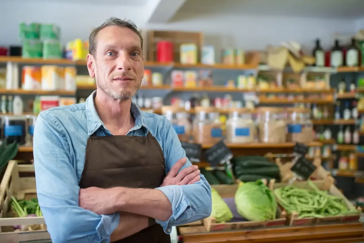 Dueño de un comercio local posando con delantal en el mostrador de su tienda